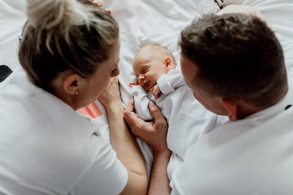 Mum and dad are laying on bed and looking at their newborn baby. Baby is sleeping. Newborn photography in Hampshire. Ewa Jones Photography