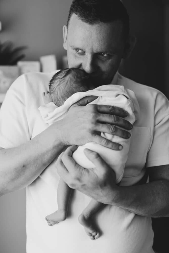 Black and white picture of dad holding a newborn baby. Newborn baby is sleeping in his arms. Newborn photography in Hampshire. Ewa Jones Photography