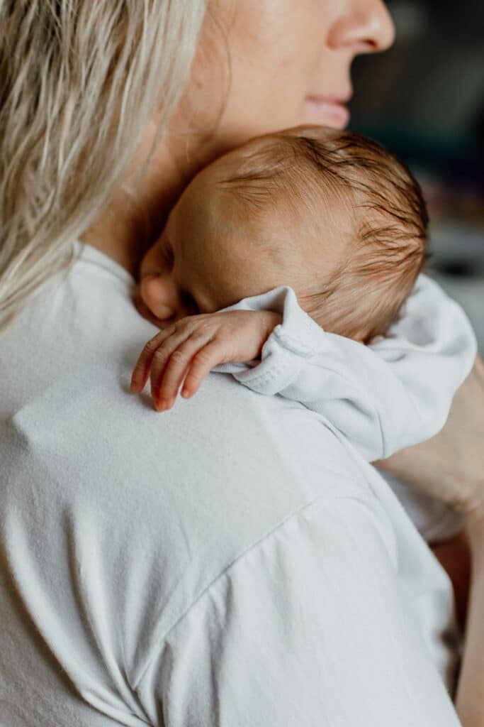 Mum is holding a newborn baby on her shoulders. Newborn baby is sleeping peacefully. Newborn photographer in Basingstoke. Ewa Jones Photography