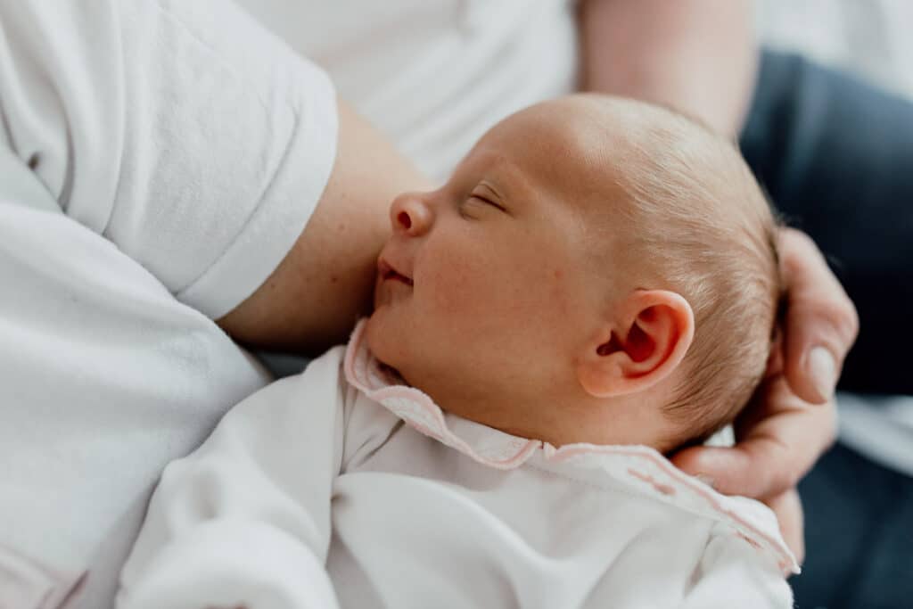 Close up detail of a newborn baby girl who is smiling. She is wearing a white body. Newborn photography in Hampshire. Ewa Jones Photography