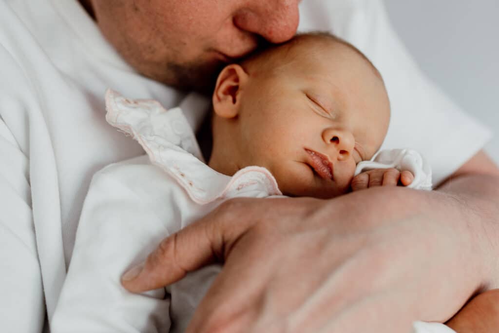 dad is kissing his newborn baby girl and holding her close to his face. Newborn baby girl is sleeping. Newborn photographer in Aldershot. Ewa Jones Photography