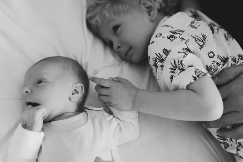 Older brother is holding little newborn brother hand. Candid black and white photography. Newborn baby photographer in Hampshire. Ewa Jones Photography