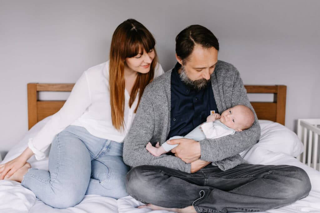 Mum and dad are sitting on the bed and looking at their newborn baby boy. Newborn photography - my first clients. Ewa Jones Photography