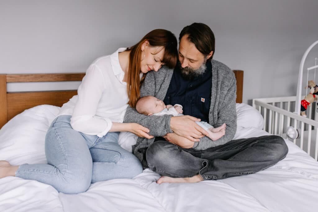 Mum and dad are sitting on the bed and looking at their newborn baby boy. Newborn photography - my first clients. Ewa Jones Photography