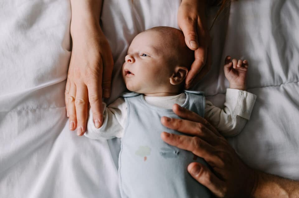 Newborn baby boy is laying on bed and mum and dad are holding him. Lovely candid photograph. Newborn photography in Basingstoke, Hampshire. Ewa Jones Photography newborn photography - my first clients