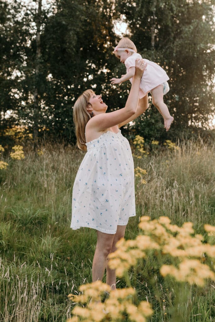 Mum is lifting her little girl up and smiling at her. Photo session during golden hour. Family photography in Basingstoke, Hampshire. Ewa Jones Photography