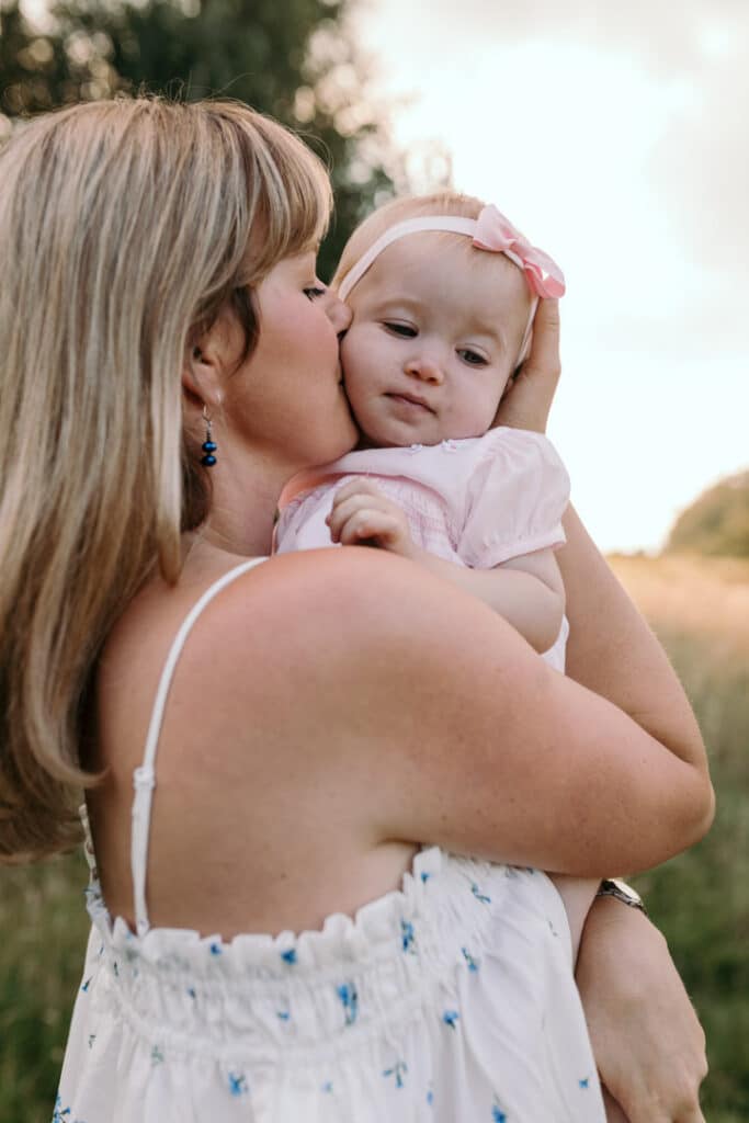 Mum is kissing her little baby girl on her cheek. Sunset family photography. Family photographer in Basingstoke, Hampshire. Ewa Jones Photography