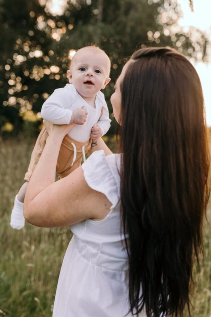 Mum is lifting up her little baby boy and he is looking at the camera and smiling. Sunset photo session in Basingstoke. Family photography in Basingstoke, Hampshire. Ewa Jones Photography