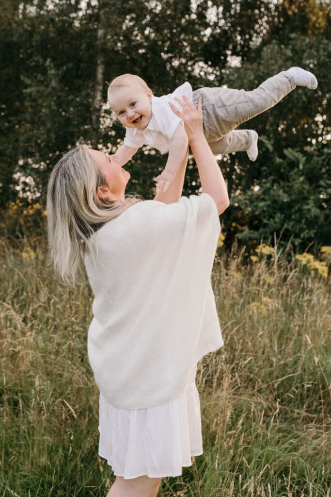 Mum is lifting up her little baby boy and he is looking at the camera and smiling. Sunset photo session in Basingstoke. Family photography in Basingstoke, Hampshire. Ewa Jones Photography