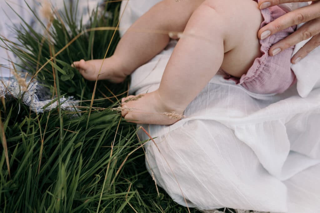 Close up detail of baby girl feet. the feet are touching the grass and the little girl is laying on mummy and breastfeeding. Family photography in Hampshire, Ewa Jones Photography