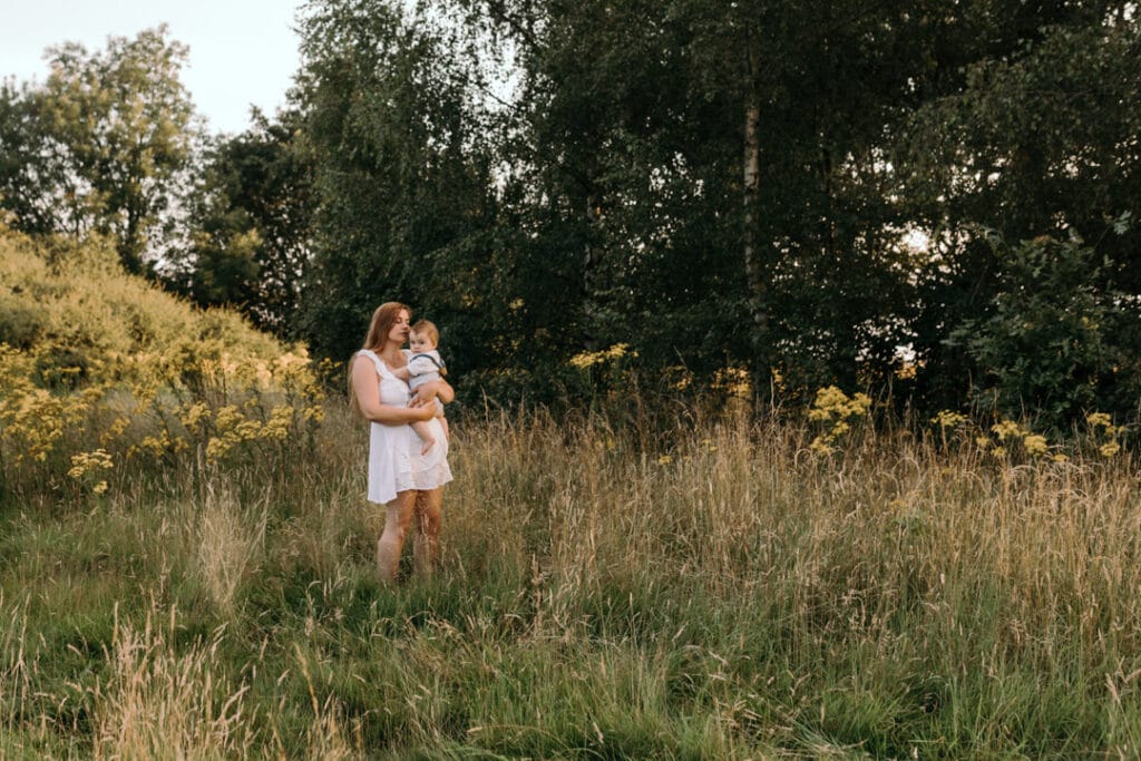 Mum is standing in the field of wild flowers and looking down at her boy. Gorgeous photo shoot in the field. Family photography in Hampshire. Ewa Jones Photography