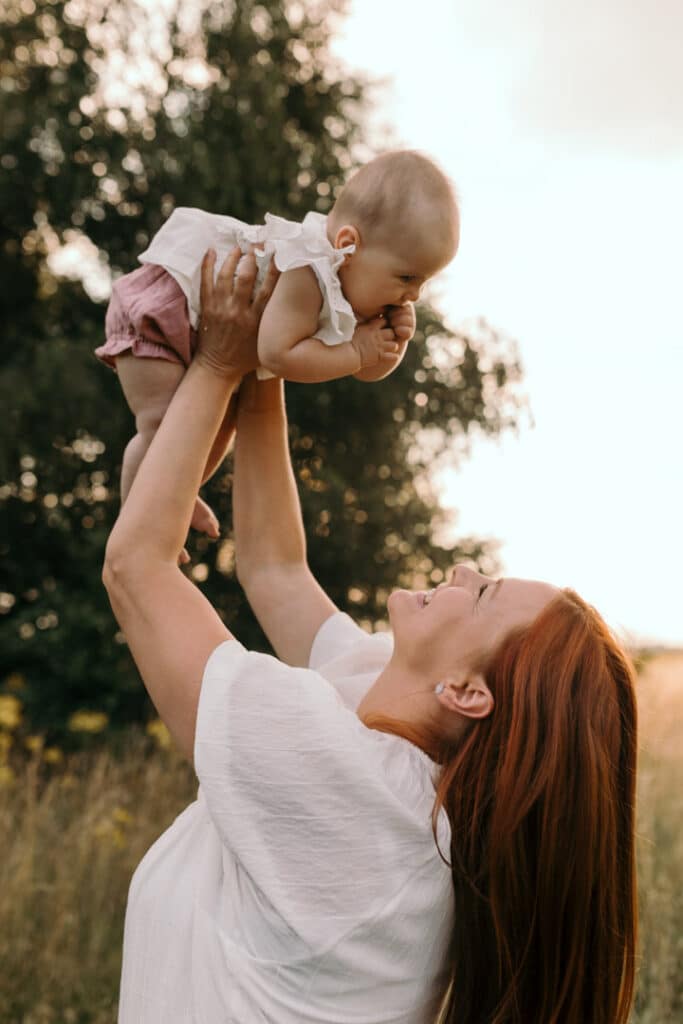 Mum is lifting her baby girl up in the air. Sunset photo shoot in the wild flowers. Family photography in Hampshire. Ewa Jones Photography