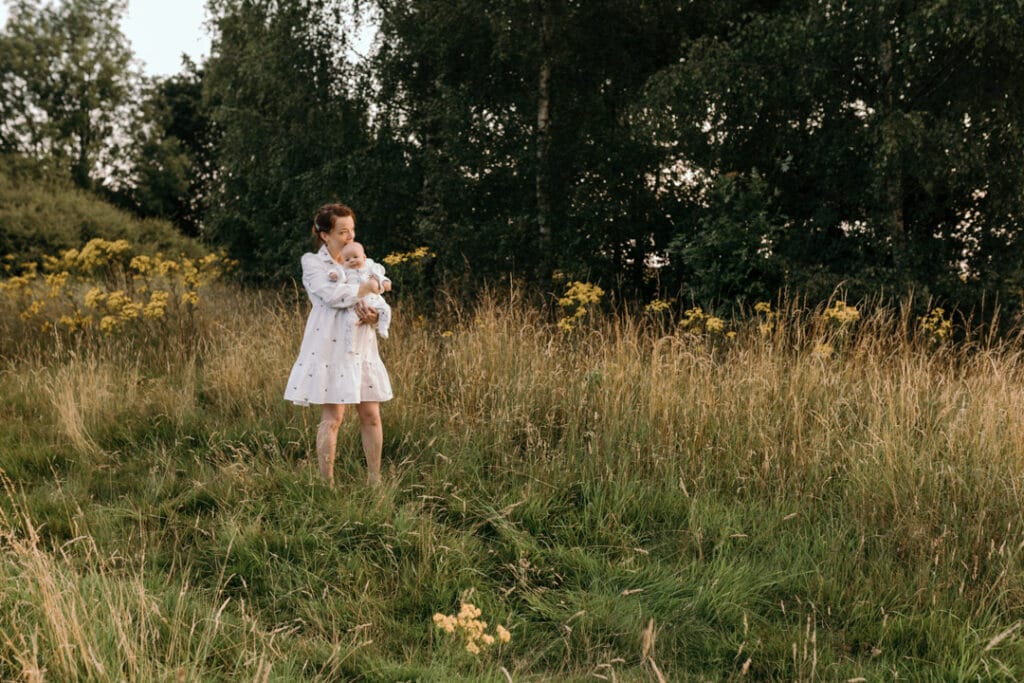 Mum is standing on the field and holding her baby boy. The little boy is looking towards camera and mum is looking at the sun. Lovely candid photo shoot. Family photographer in Hampshire. Ewa Jones Photography