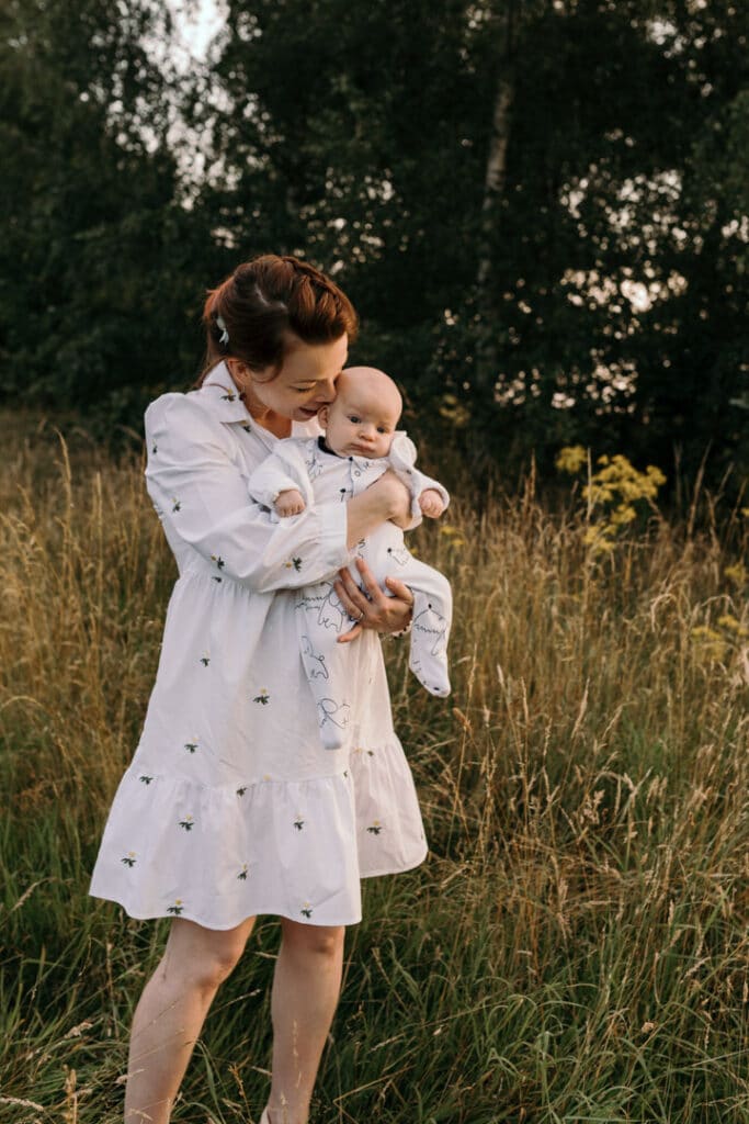 Mum is cuddling her baby boy. Mum is wearing lovely white dress with white daisies. Sunset photo shoot in the wild flower field. Family photography in Basingstoke, Hampshire. Ewa Jones Photography