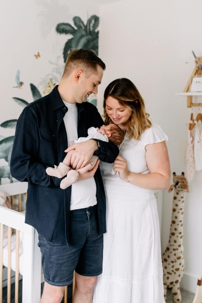 Mum and dad are standing in a lovely safari theme nursery and holding their newborn baby girl in their arms. Newborn photographer in Basingstoke, Ewa Jones Photography