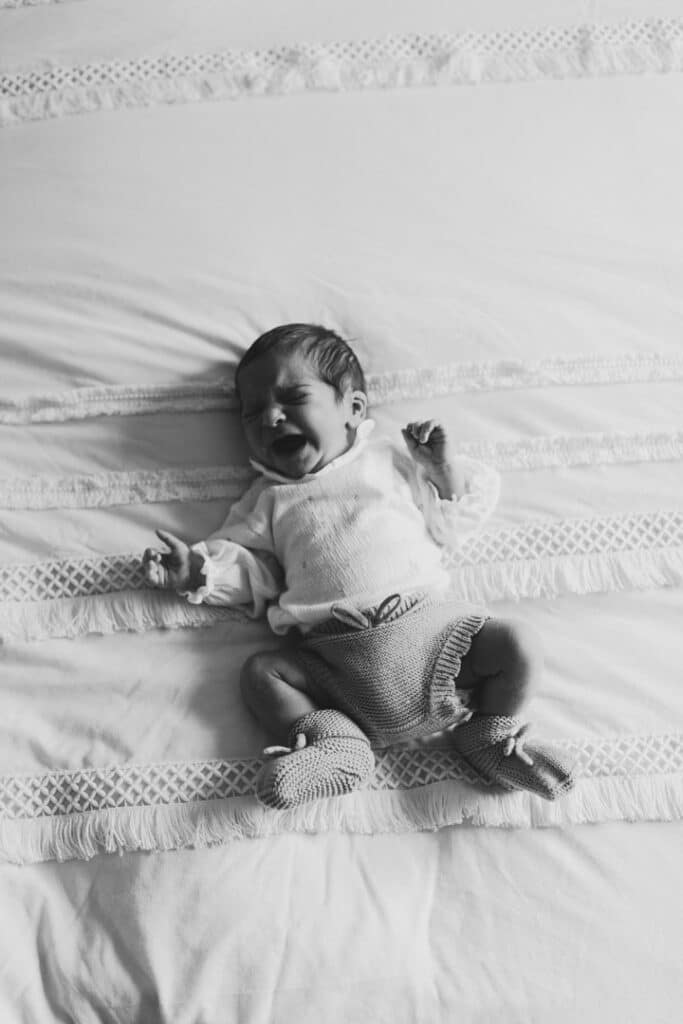 Newborn baby girl is laying on bed and crying. Newborn photo session in Basingstoke, Hampshire. Ewa Jones Photography