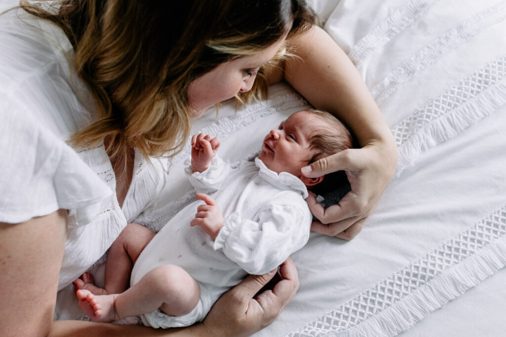 Mum is laying on the bed with her newborn baby girl. Newborn baby girl is looking at her mum. Newborn photography in Hampshire. Ewa Jones Photography