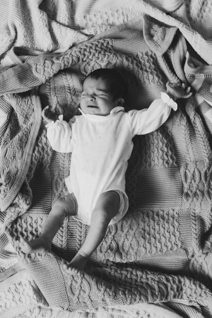 Baby girl is laying on blankets and raising her hands up. Newborn baby photoshoot in Basingstoke, Hampshire. Ewa Jones photography