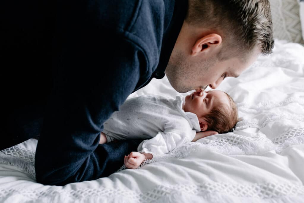 Newborn baby girl is sleeping on bed and dad is kissing her baby girl on her nose. Lovely in home candid newborn photography in Basingstoke, Hampshire.