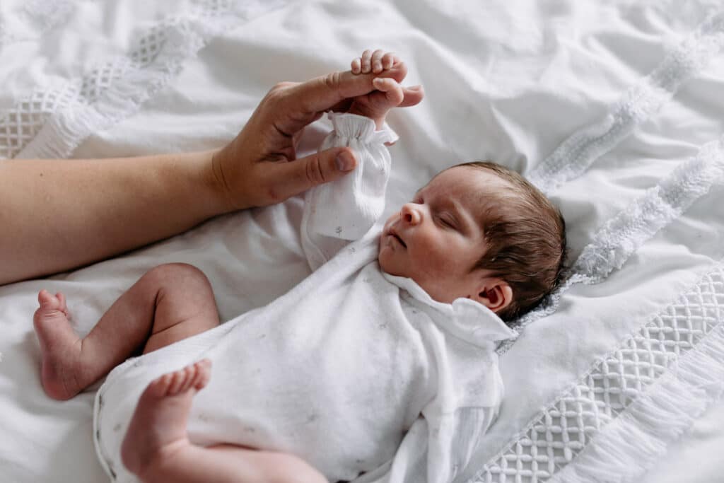 Newborn baby girl is laying on bed sleeping. she is also holding mummy's finger. Newborn photographer in Hampshire. Ewa Jones Photography