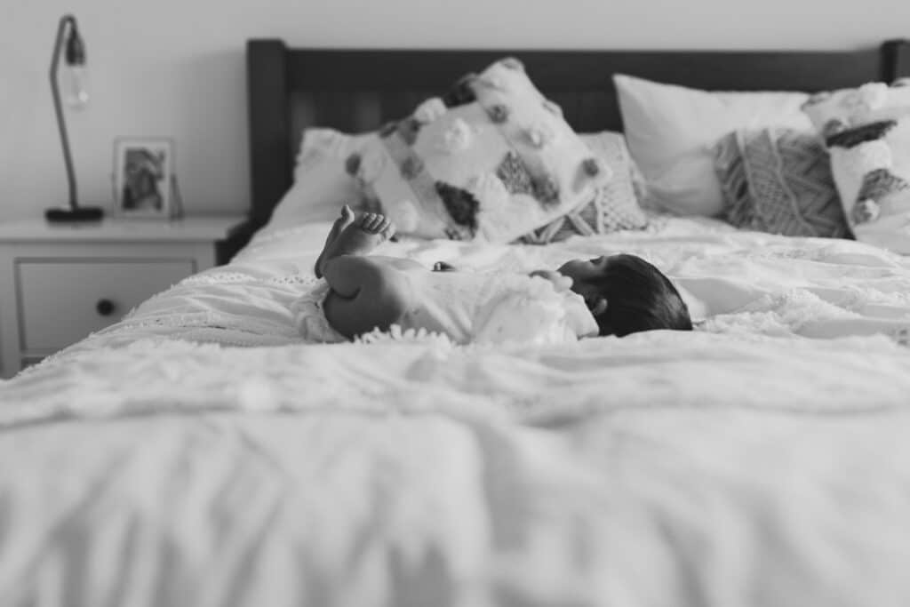 Newborn baby girl is laying on the bed. Black and white photograph. Newborn photoshoot in Basingstoke, Hampshire. Ewa Jones Photography