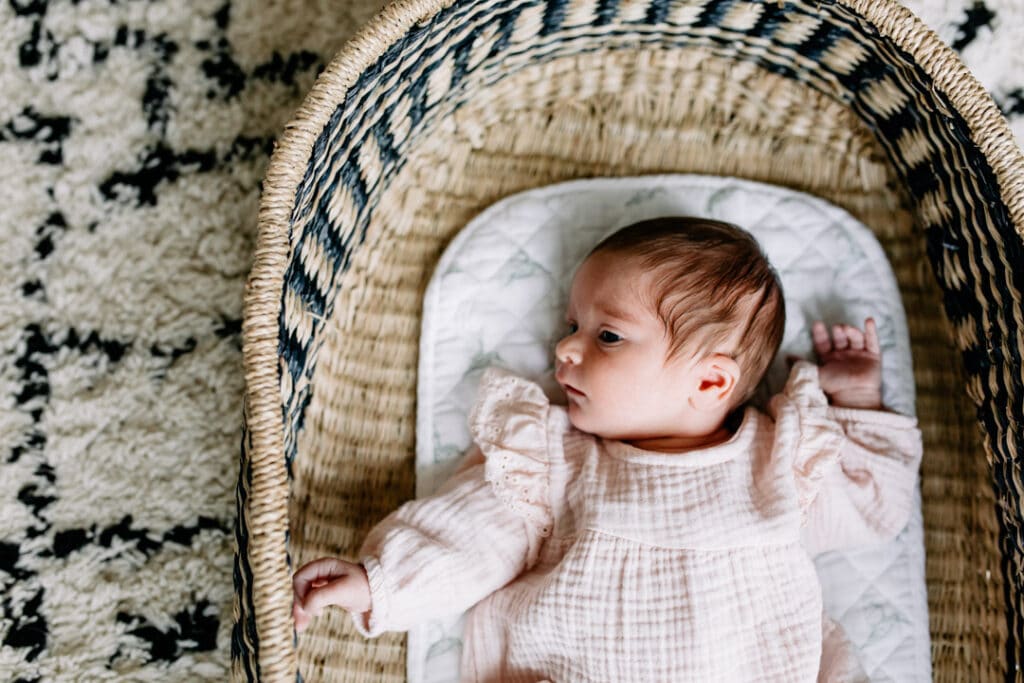 Newborn baby girl is laying inside her moses basket and looking up. In home newborn photography in Hampshire. Ewa Jones Photography