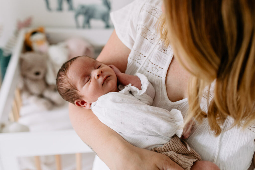 Mum is holding her newborn baby girl. Lovely natural light is coming through the windows. Newborn photographer in Hampshire. Ewa Jones Photography