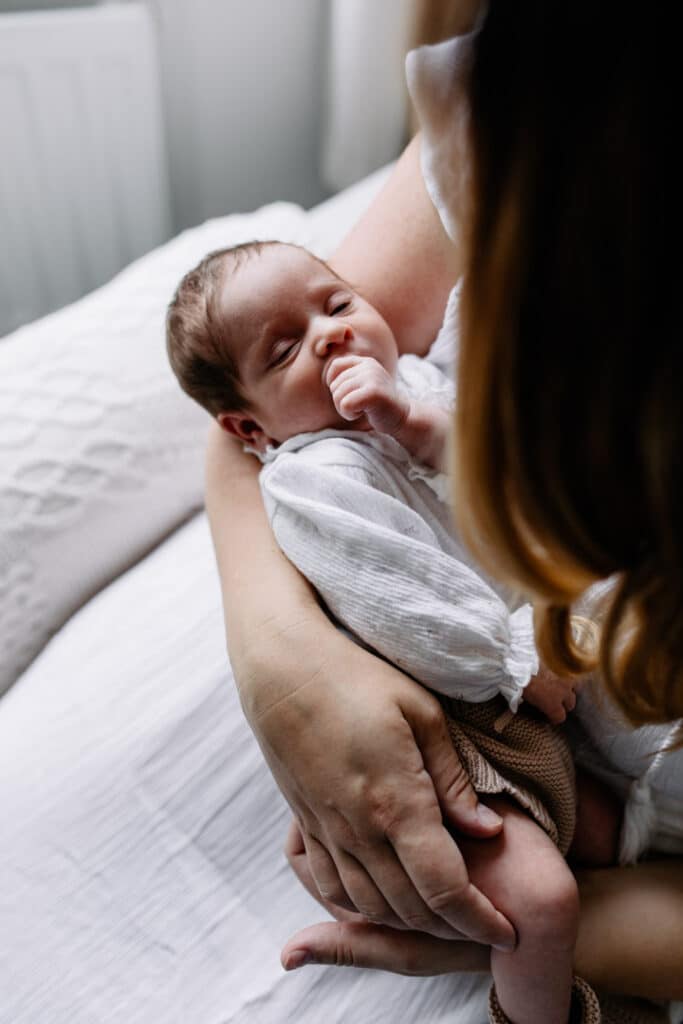 Mum is holding her newborn baby girl. Lovely natural light is coming through the windows. Newborn photographer in Hampshire. Ewa Jones Photography