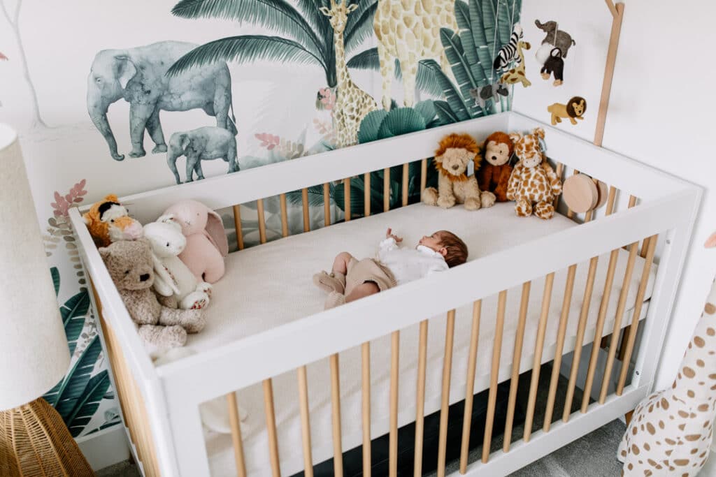 Newborn baby girl is laying in her cot in her beautiful jungle theme nursery. Newborn photo shoot in Hampshire. Ewa Jones Photography