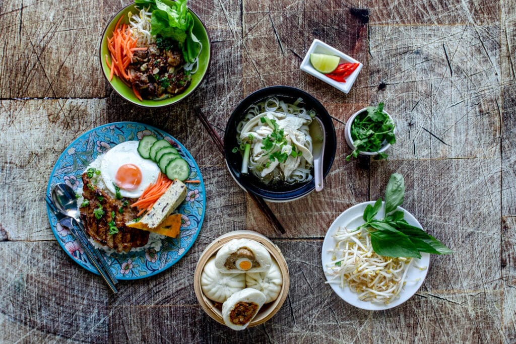 Various Vietnamese food on the wooden table including chicken noodle soup, buns, stir fry. Food photography in Basingstoke, Hampshire. Ewa Jones Photography