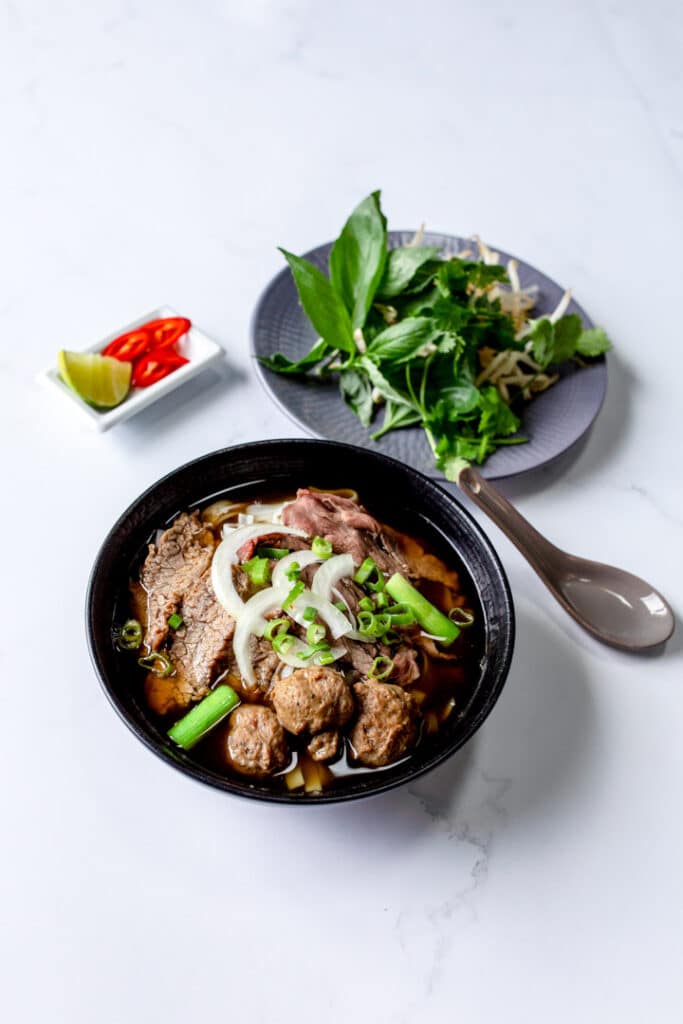 Beeg noodle soup, pho bo Vietnamese food in black bowl with herbs. Product photography in Hampshire. Ewa Jones Photography