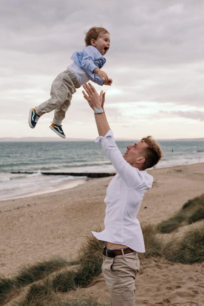 Dad is throwing his little boy in the air and the little boy is laughing. Family photographer in Hampshire. Ewa Jones Photography