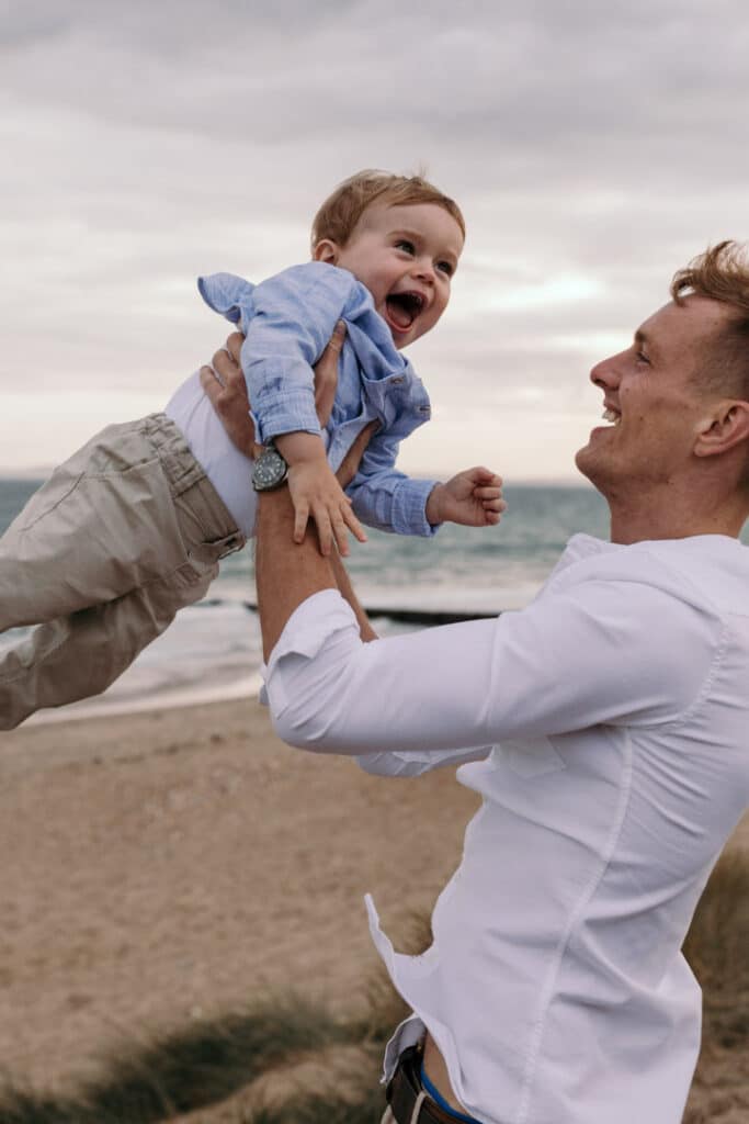 Dad is throwing his little boy in the air and the little boy is laughing. Family photographer in Hampshire. Ewa Jones Photography