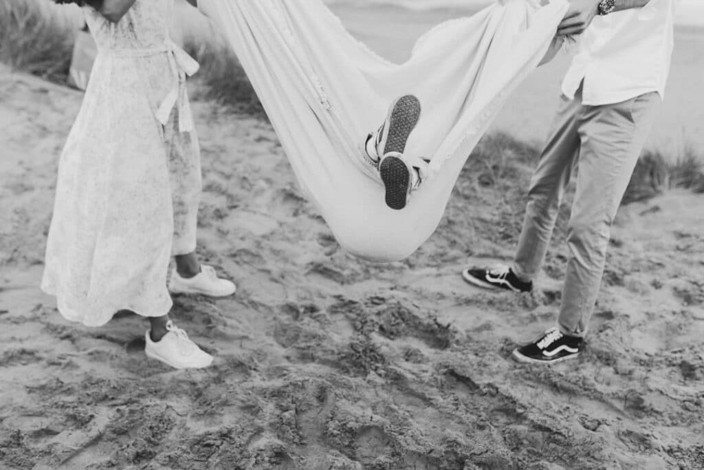 black and white detail shot of little boy feet poking through the blanket. Mum and dad are swinging him. family photo session at the beach. Ewa Jones Photography