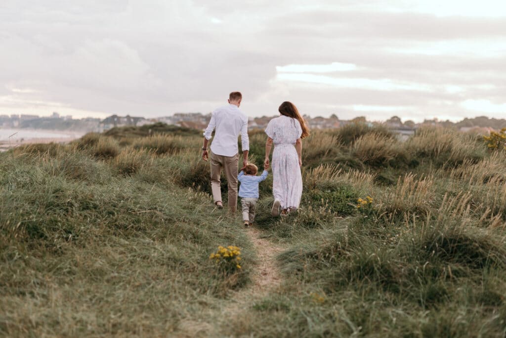 Family of three is walking away from the photographer and walking on the sand dunes. Family photographer in Hampshire. Ewa Jones Photography