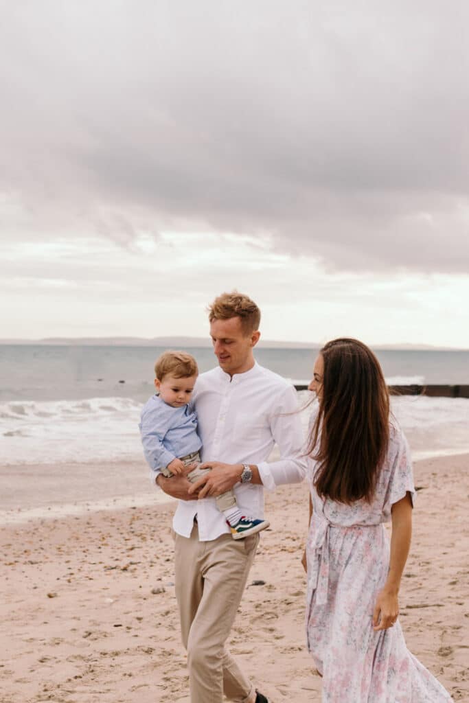 mum and dad are walking on the beach and dad is holding his little boy. Lovely sunset family photo session at the beach. Hampshire family photographer. Ewa Jones Photography
