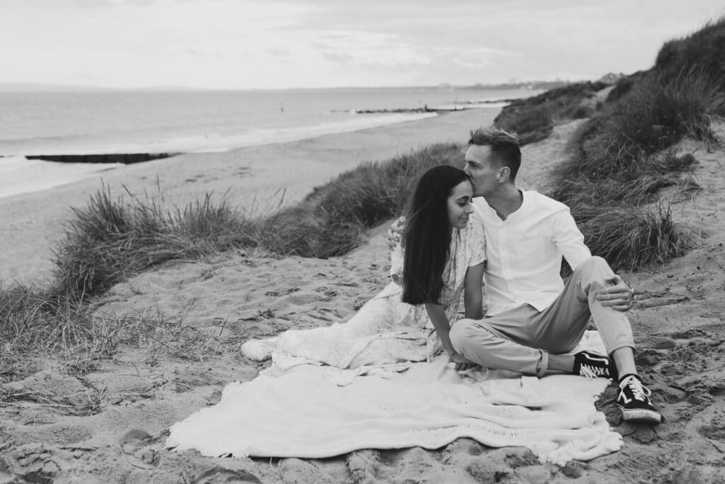 Mum and dad are sitting on the blanket and dad is kissing his partner on her head. Lovely romantic couple image. Photographer in Hampshire. Ewa Jones Photography