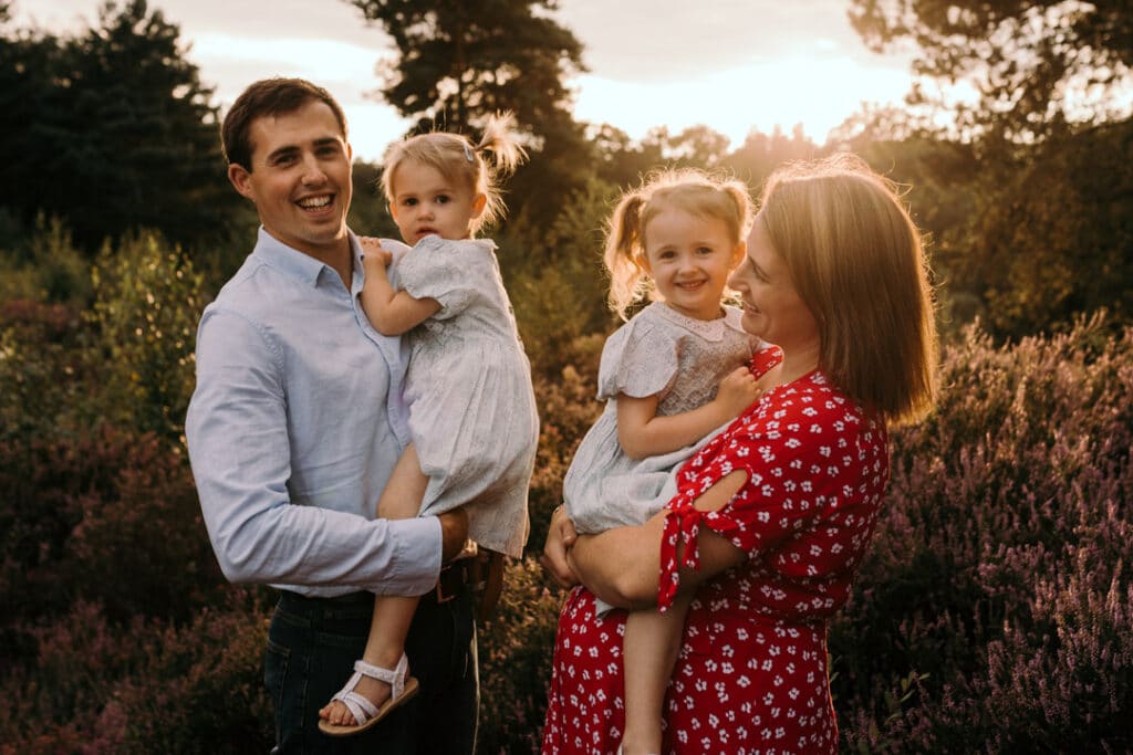 family of four is laughing and mum is looking at her husband and younger daughter and the older daughter is looking at the camera. Golden hour maternity photography in Hampshire. Ewa Jones Photography