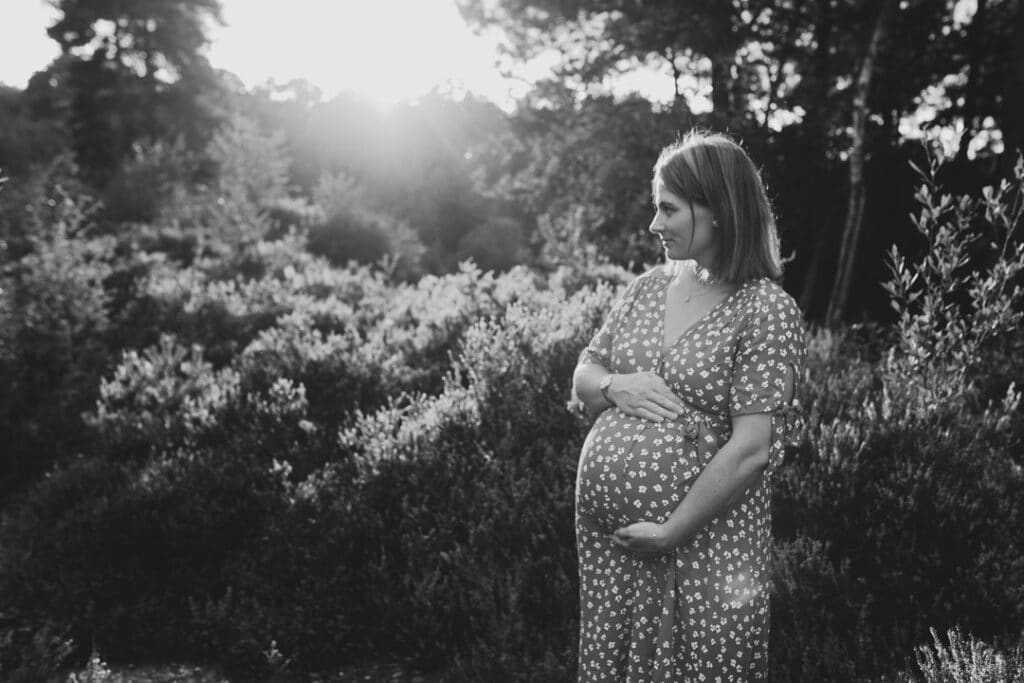 Expecting mum is looking away and holding her baby bump. it's a lovely summer evening and sun is shining behind expecting mum. maternity photographer in Basingstoke, Hampshire. Ewa Jones Photography