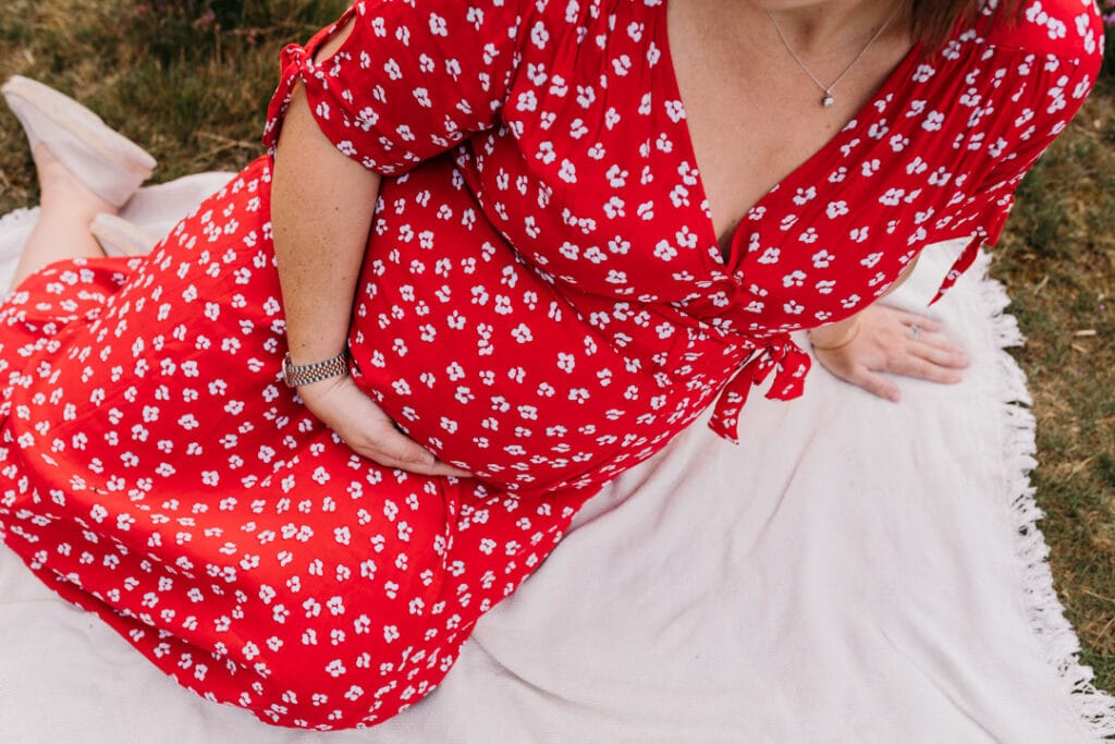 close up picture of expecting mum bump. Mum is wearing lovely red dress with white flowers. maternity photography in Basingstoke, Hampshire. Ewa Jones Photography