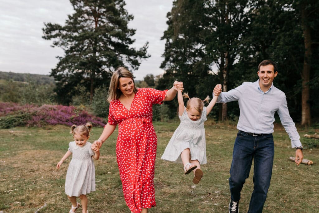 Family of four are walking towards the camera and mum and dad are swinging their younger daughter. lovely family photo session in Hampshire. Family photographer in Hampshire. Ewa Jones Photography