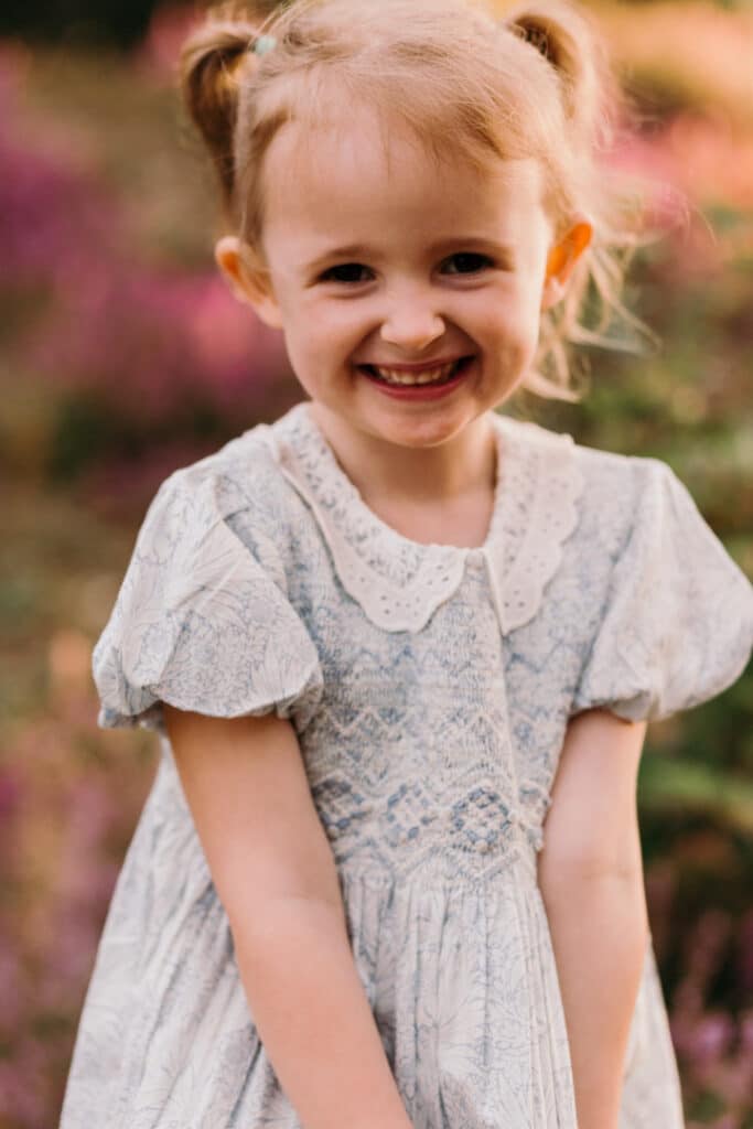 Little girl is wearing a lovely blue and white flower dress. she has two ponytails and looking at the camera. Lovely sunset and golden hour photo session. Family photography in Hampshire, Ewa Jones Photography