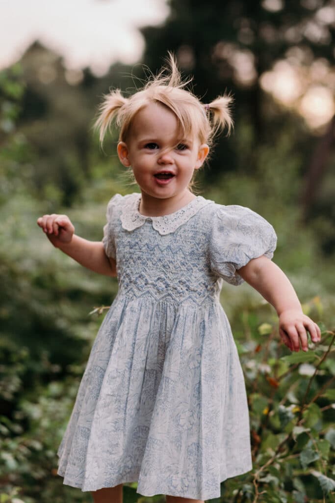 Little girl is wearing a lovely blue and white flower dress. she has two ponytails and looking at her parents. Lovely sunset and golden hour photo session. Family photography in Hampshire, Ewa Jones Photography