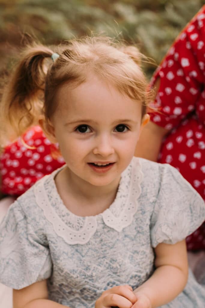 Little girl is looking at the camera. she is wearing lovely blue dress and has two ponytails. Lovely family photo sessions in Hampshire. Ewa Jones Photography