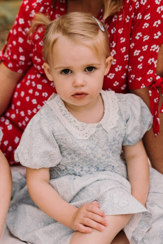 Little girl is looking at the camera. she is wearing lovely blue dress and has two ponytails. Lovely family photo sessions in Hampshire. Ewa Jones Photography