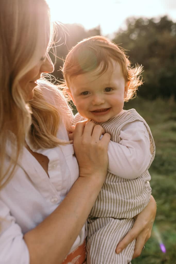 Mum is holding her baby in her arms and looking at him. Boy is wearing lovely stripy outfit. Summer family photo shoot in Hampshire. Ewa Jones Photography