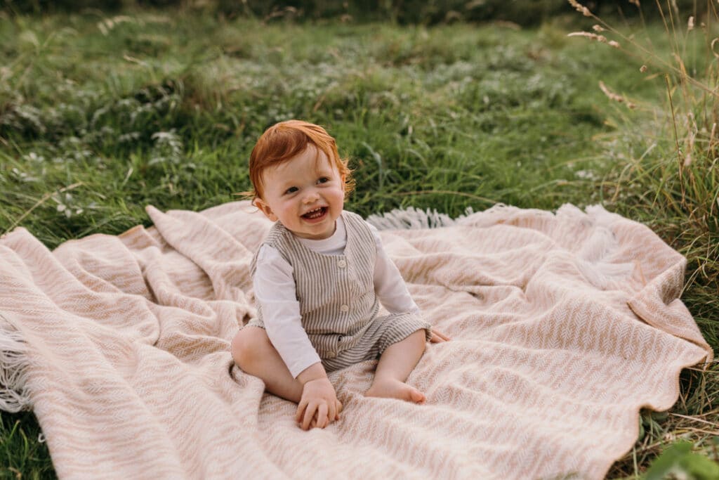 boy is sitting on the blanket and looking away. he is wearing lovely stripy outfit. Natural family photo shoot in Hampshire. Ewa Jones Photography