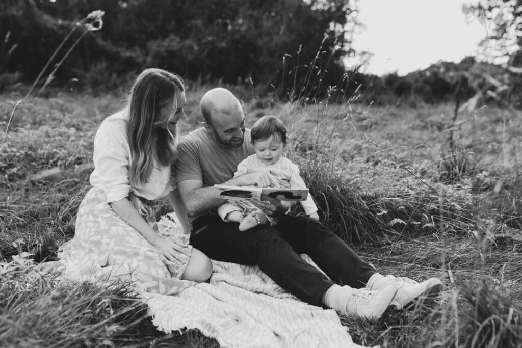family photo session in Hampshire. family are sitting on the grass and reading book. black and white image of family. family photo session at the sunset. family photographer in Hampshire. Ewa Jones Photography