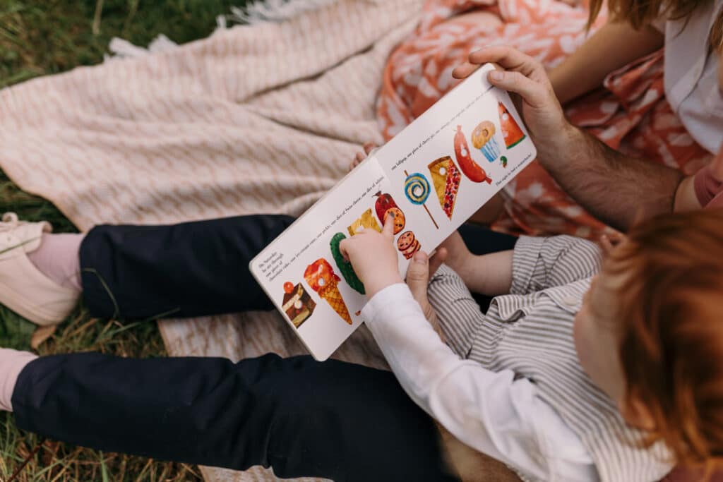 Little boy is reading the book and pointing at the image in the book. Natural lifestyle family photo session in Hampshire. Ewa Jones Photography