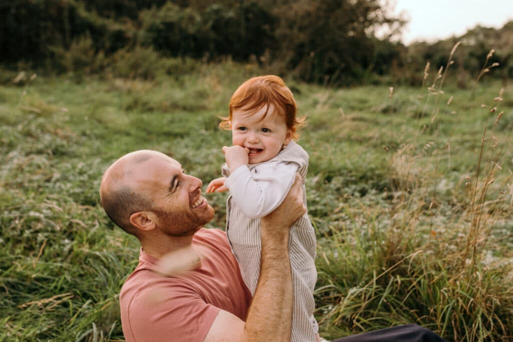 little boy is smiling and looking at his mum. dad is looking at the boy as well. Family photo shoot at the field during golden hour. Family photo session in Hampshire. Ewa Jones Photography